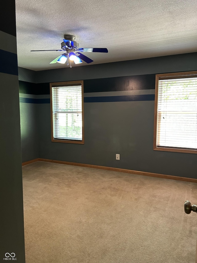 carpeted empty room with a textured ceiling, ceiling fan, healthy amount of natural light, and baseboards