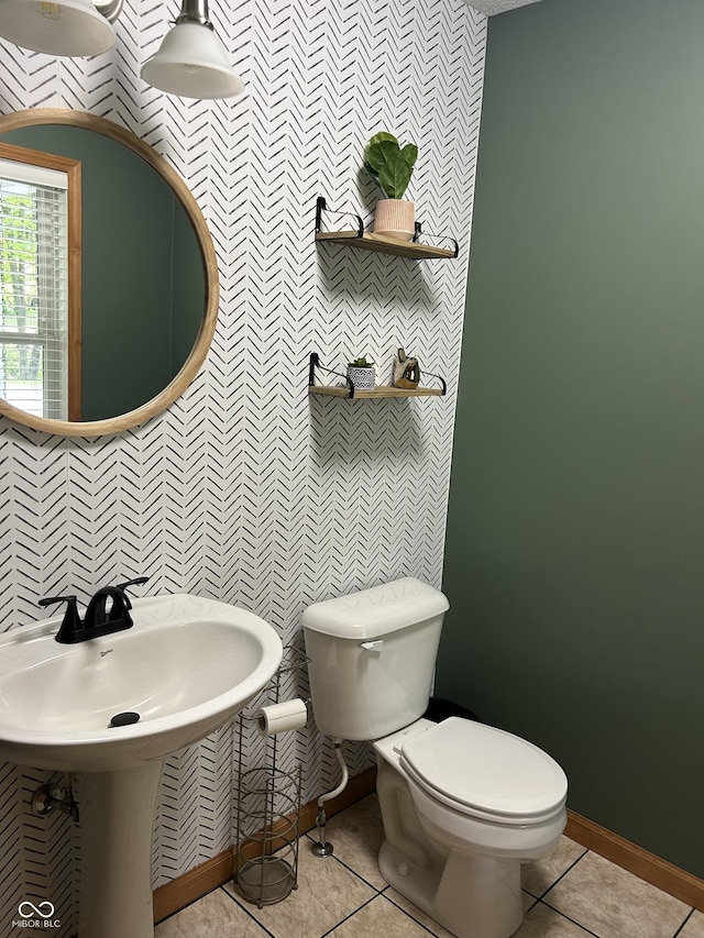 bathroom featuring wallpapered walls, toilet, tile patterned floors, baseboards, and an accent wall