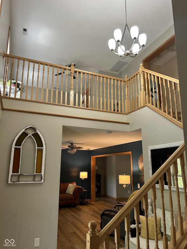 staircase with a towering ceiling, wood finished floors, ceiling fan, and a chandelier