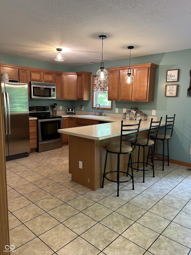 kitchen with stainless steel appliances, a peninsula, light countertops, a sink, and a textured ceiling