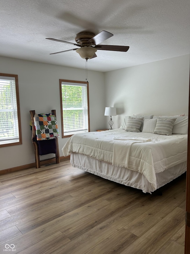 bedroom with wood finished floors, baseboards, a textured ceiling, and a ceiling fan