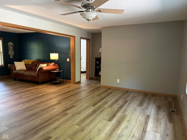 living room featuring light wood-type flooring, ceiling fan, baseboards, and a textured ceiling