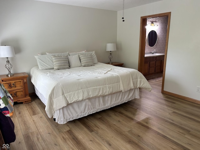 bedroom featuring wood finished floors, a sink, connected bathroom, and baseboards