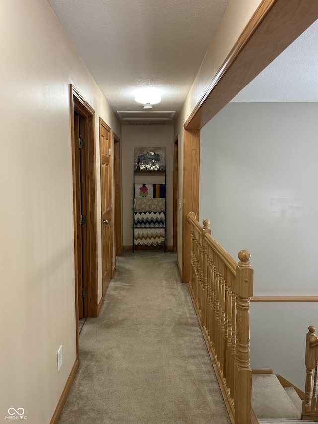 hall with an upstairs landing, light carpet, and a textured ceiling