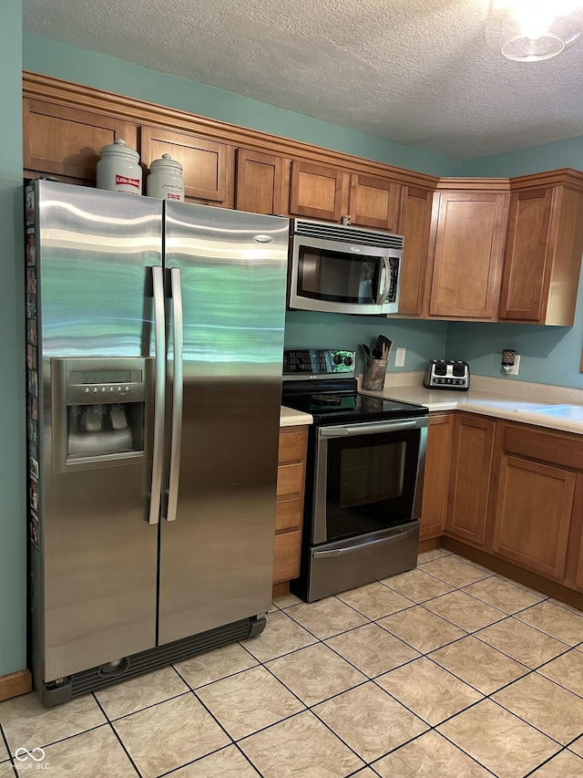 kitchen with appliances with stainless steel finishes, light countertops, a textured ceiling, brown cabinets, and light tile patterned flooring