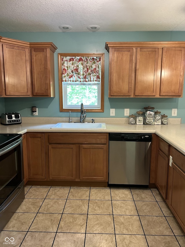 kitchen featuring appliances with stainless steel finishes, a sink, light countertops, a textured ceiling, and brown cabinets