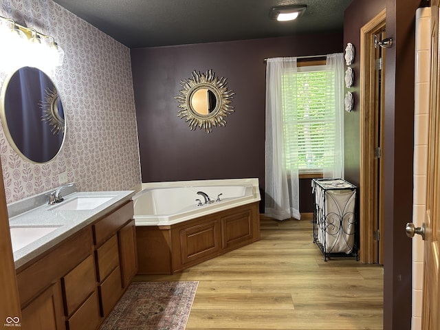 bathroom with wallpapered walls, wood finished floors, a bath, and double vanity