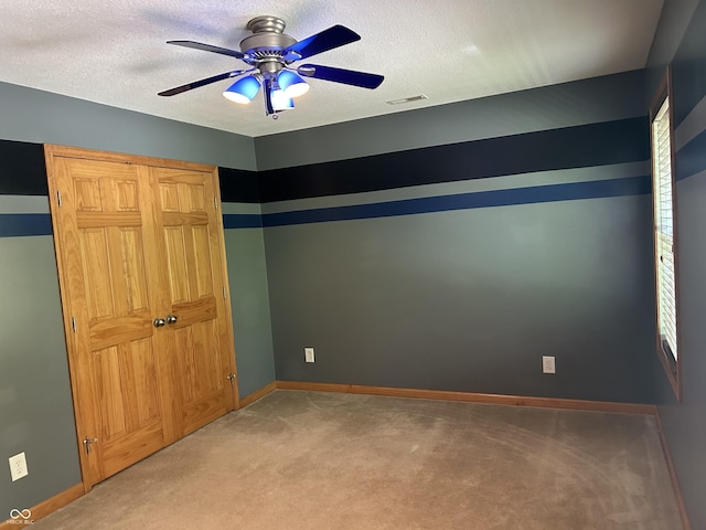 unfurnished bedroom with light colored carpet, a textured ceiling, baseboards, and a ceiling fan