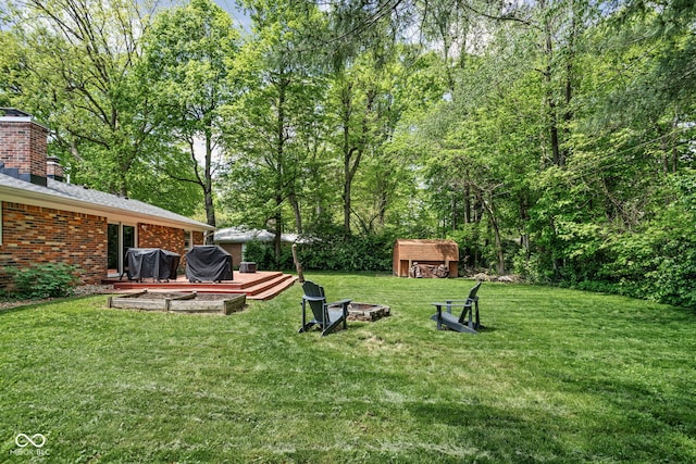 view of grassy yard featuring a shed, a fire pit, an outdoor structure, and a wooden deck