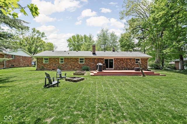 back of house with a fire pit, a deck, a chimney, a yard, and brick siding