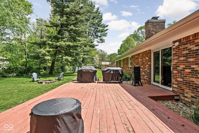 deck featuring an outdoor fire pit, a yard, grilling area, and view of wooded area