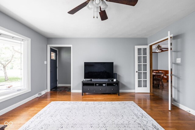 living area with a ceiling fan, wood finished floors, baseboards, and french doors