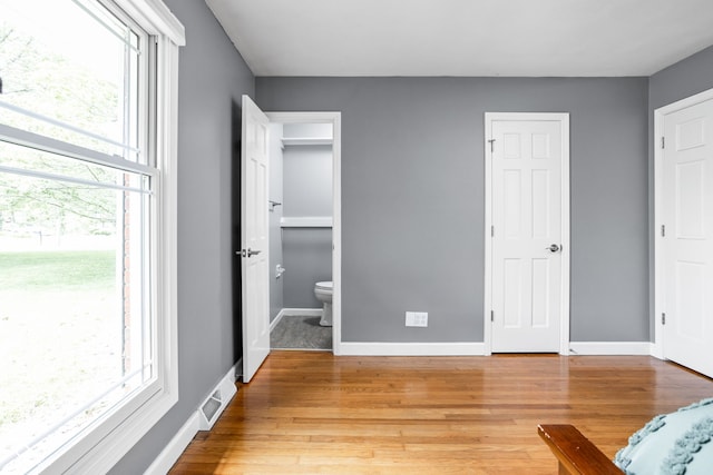 unfurnished bedroom with multiple windows, light wood-style flooring, and baseboards