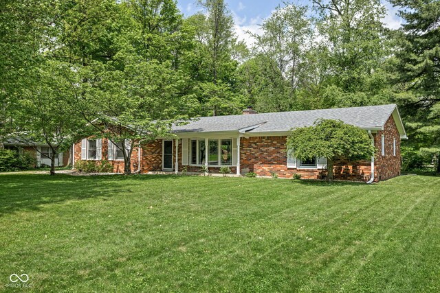 view of front facade featuring a front lawn, brick siding, a chimney, and roof with shingles