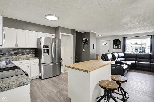 kitchen featuring stainless steel fridge with ice dispenser, open floor plan, butcher block counters, a kitchen bar, and light wood-style flooring
