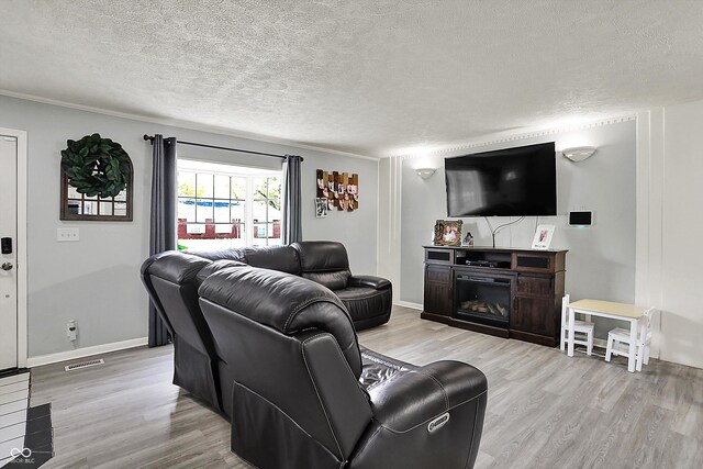 living room featuring wood finished floors, a textured ceiling, a glass covered fireplace, and baseboards