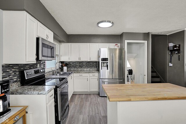 kitchen with appliances with stainless steel finishes, a sink, wood counters, white cabinets, and a textured ceiling
