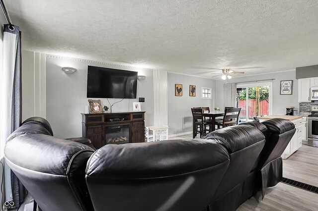 living area featuring light wood-style floors, a textured ceiling, and ceiling fan