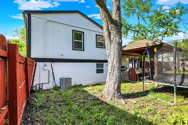 back of house with a trampoline, a fenced backyard, cooling unit, and board and batten siding
