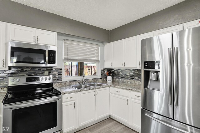 kitchen featuring appliances with stainless steel finishes, a sink, white cabinetry, light wood-type flooring, and a textured ceiling