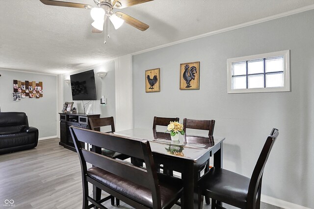 dining space with ceiling fan, light wood-type flooring, a textured ceiling, baseboards, and ornamental molding