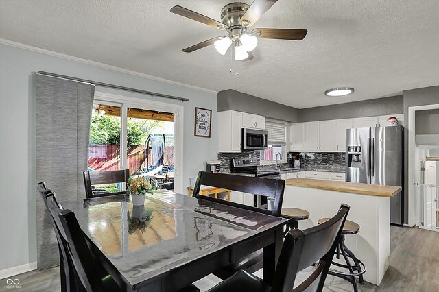 dining area featuring light wood-type flooring, crown molding, a textured ceiling, a ceiling fan, and baseboards