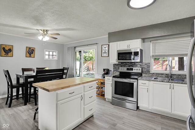 kitchen with stainless steel appliances, butcher block counters, a sink, white cabinets, and a ceiling fan