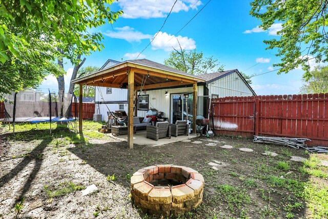 fenced backyard featuring a trampoline, an outdoor living space with a fire pit, and a patio