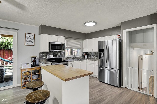 kitchen featuring stainless steel appliances, butcher block counters, light wood-style flooring, a sink, and tasteful backsplash