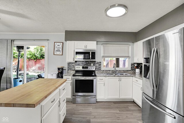 kitchen featuring appliances with stainless steel finishes, a sink, butcher block counters, light wood finished floors, and decorative backsplash
