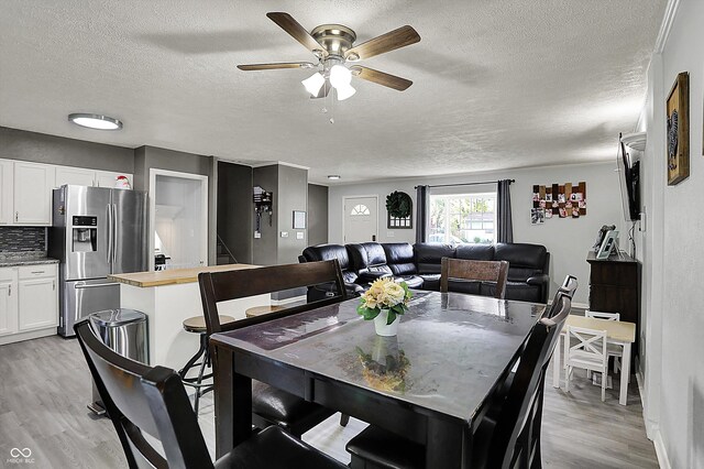 dining space featuring a textured ceiling, light wood-style flooring, ceiling fan, and baseboards