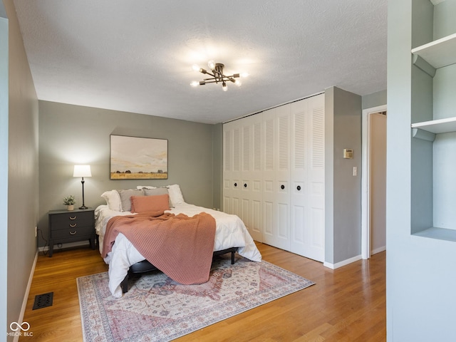 bedroom featuring wood finished floors, baseboards, a closet, a chandelier, and a textured ceiling