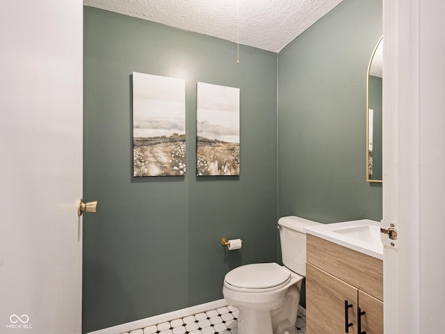 half bathroom featuring a textured ceiling, toilet, vanity, and baseboards