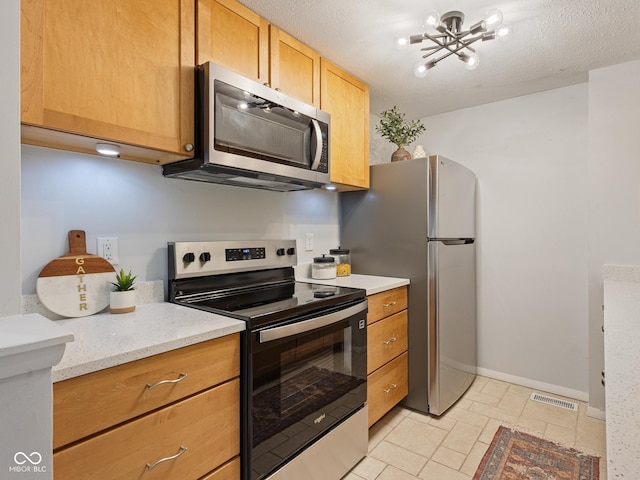 kitchen featuring appliances with stainless steel finishes, a chandelier, baseboards, and a textured ceiling