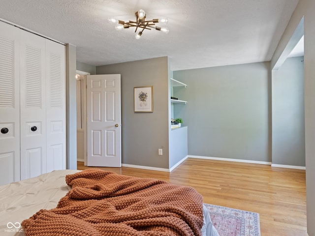 bedroom featuring light wood-type flooring, a closet, baseboards, a textured ceiling, and a chandelier