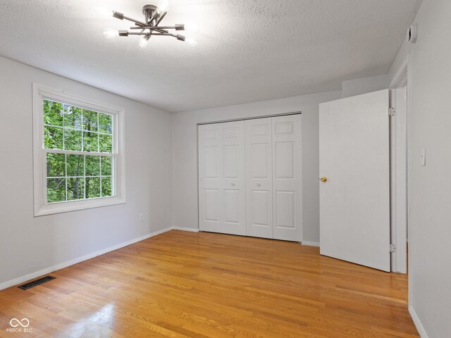 unfurnished bedroom featuring light wood-style flooring, baseboards, a textured ceiling, and a closet