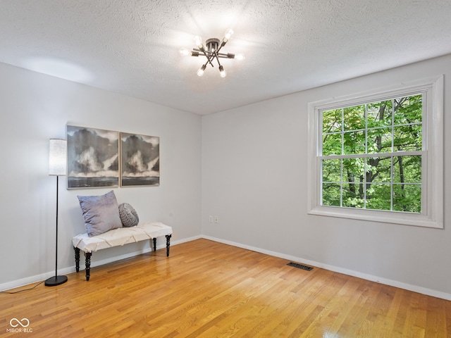 sitting room with light wood-style floors, a chandelier, baseboards, and a textured ceiling