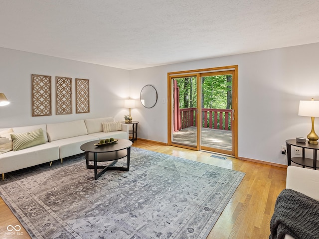 living room featuring baseboards, light wood finished floors, and a textured ceiling
