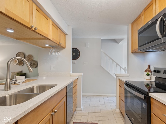 kitchen featuring appliances with stainless steel finishes, a sink, light stone counters, baseboards, and a textured ceiling