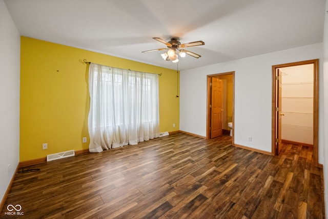 unfurnished bedroom with dark wood-type flooring, baseboards, a walk in closet, a closet, and a ceiling fan