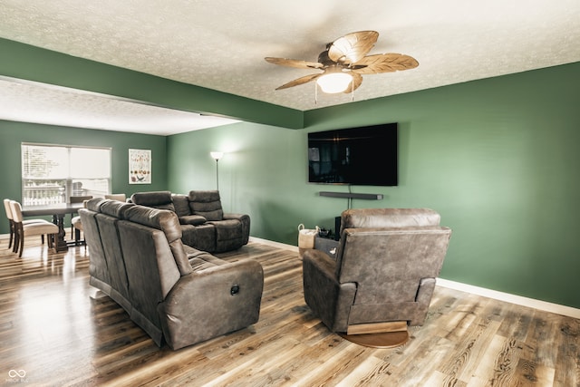 living room with a textured ceiling, wood finished floors, baseboards, and ceiling fan