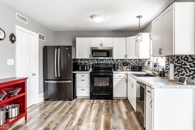 kitchen featuring appliances with stainless steel finishes, a sink, backsplash, light wood-style floors, and white cabinetry