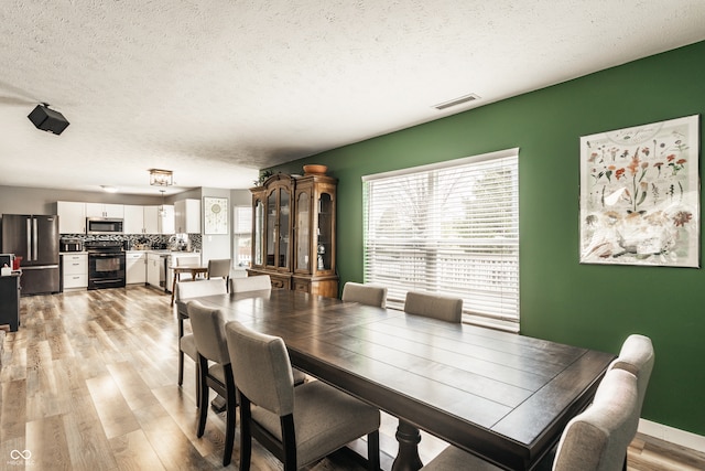 dining area with a textured ceiling, light wood-style flooring, and baseboards