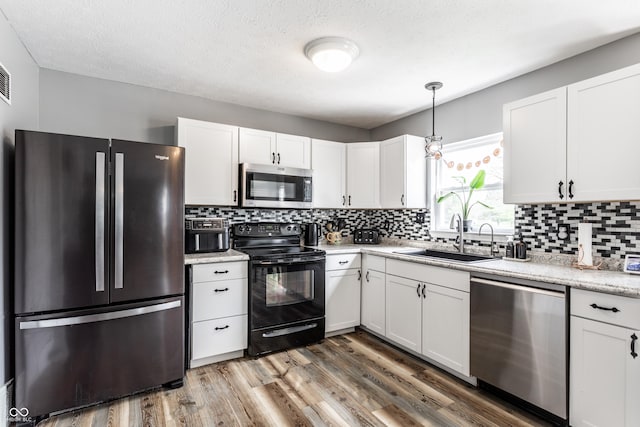 kitchen with appliances with stainless steel finishes, a sink, decorative backsplash, white cabinetry, and a textured ceiling