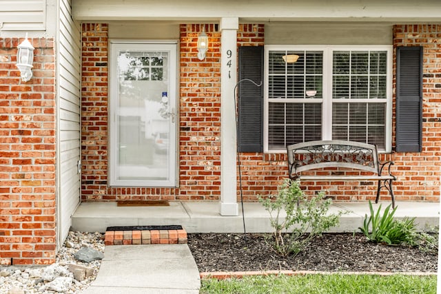 view of exterior entry with brick siding and a porch