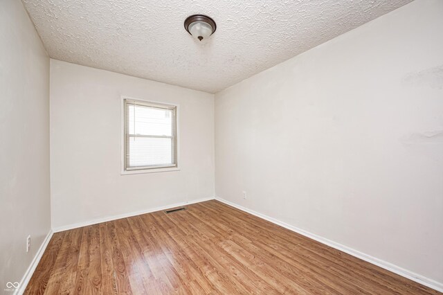 empty room with wood finished floors, a textured ceiling, and baseboards