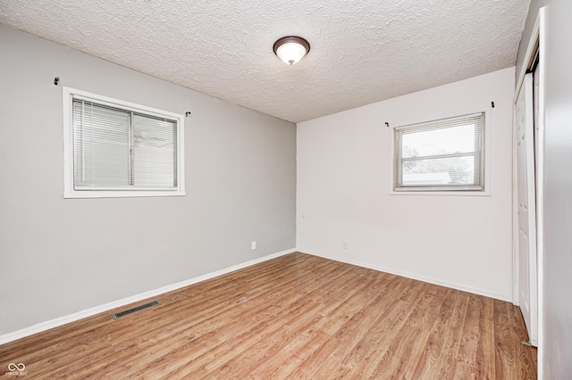 empty room featuring light wood finished floors, baseboards, and a textured ceiling