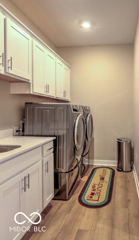 clothes washing area featuring cabinet space, washing machine and dryer, wood finished floors, recessed lighting, and baseboards