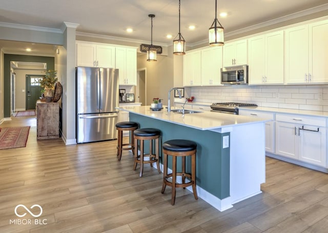 kitchen featuring appliances with stainless steel finishes, a sink, a kitchen breakfast bar, an island with sink, and ornamental molding