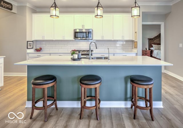 kitchen with stainless steel microwave, a breakfast bar area, light wood-type flooring, a sink, and ornamental molding